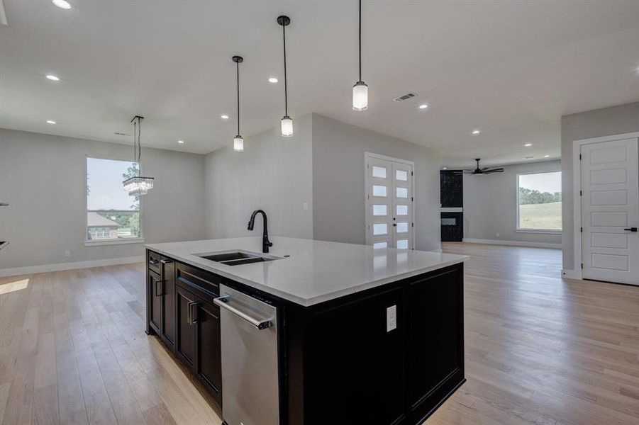 Kitchen island with a white countertop and dark cabinetry, integrated sink with a matte black faucet, recessed lighting, and wood-finish flooring