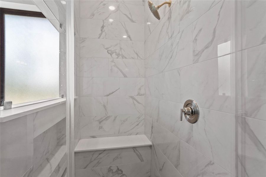 Enjoy a spa-like experience in this modern walk-in shower with built-in seat, niche for shower supplies, fixed shower head and elegant porcelain tile surround.