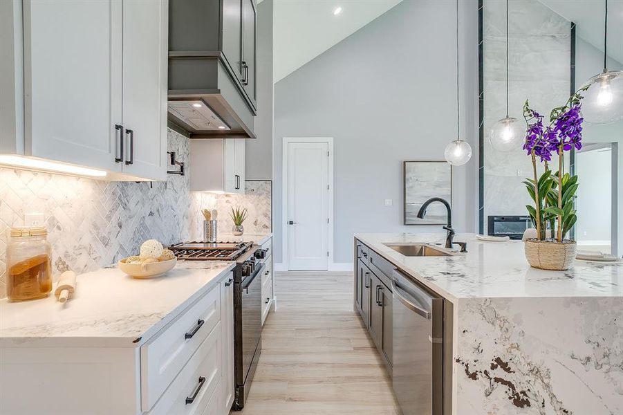 Kitchen with light stone counters, black gas stove, white cabinetry, backsplash, and hanging light fixtures