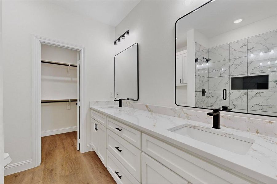 Bathroom with a marble finish shower, light wood-type flooring, double vanity, and a spacious closet