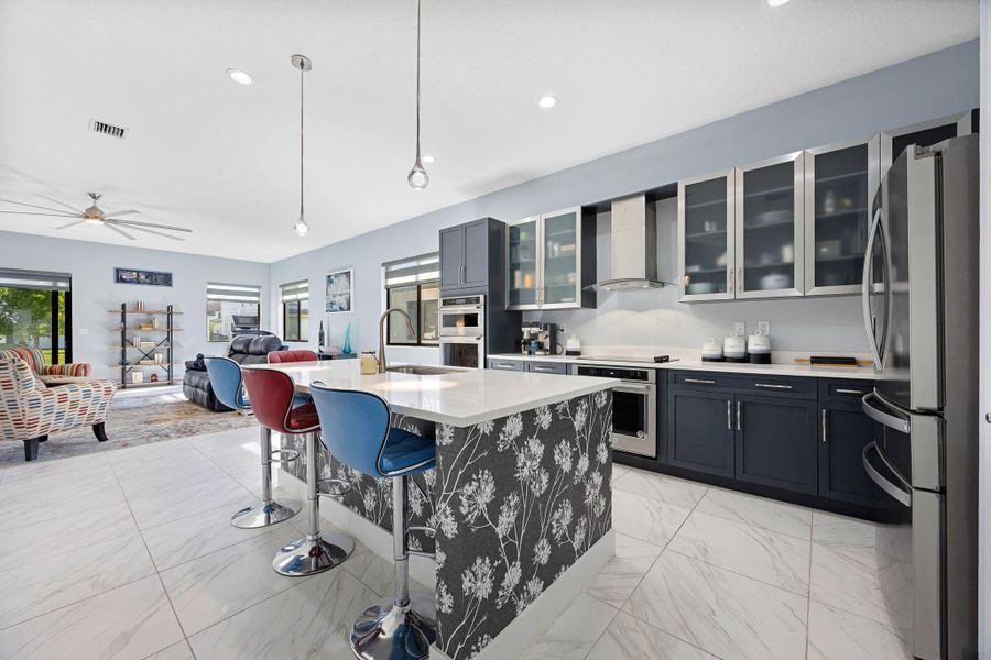 Kitchen featuring decorative light fixtures, glass insert cabinets, appliances with stainless steel finishes, a breakfast bar area, and an island with sink