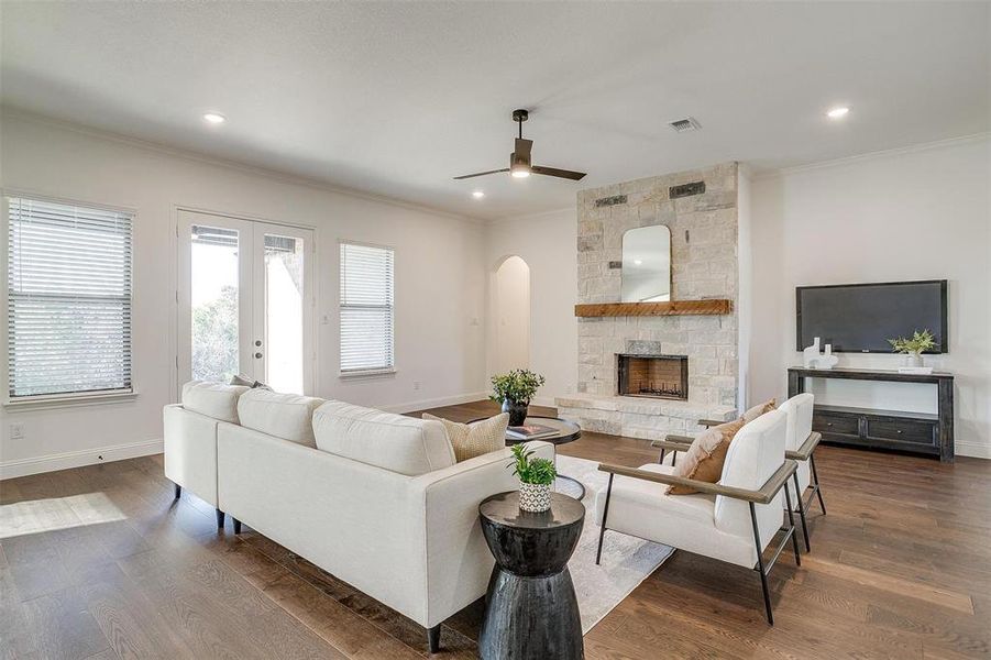 Living room featuring fireplace with stone surround, crown molding, ceiling fan, engineered wood flooring, 10 ft ceilings and 8 ft doors