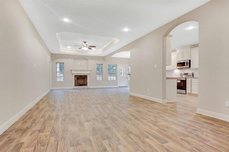 This spacious living area features wood-look flooring, a cozy fireplace, and ample natural light from multiple windows. The open layout seamlessly connects to a modern kitchen with stainless steel appliances and white cabinetry, creating an inviting space for entertaining. This spacious living area features wood-look flooring, a cozy fireplace, and ample natural light from multiple windows. The open layout seamlessly connects to a modern kitchen with stainless steel appliances and white cabinetry, creating an inviting space for entertaining.