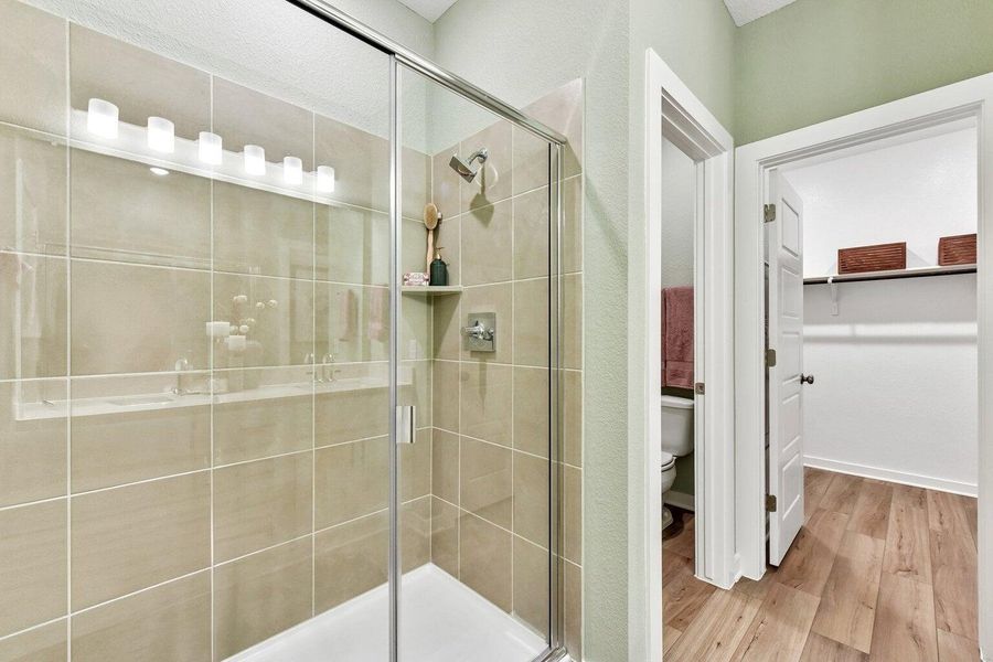 A well-lit, tiled shower with a glass enclosure adjoins a spacious walk-in closet.