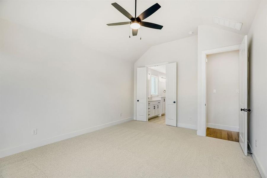 Carpeted room featuring a vaulted ceiling with a ceiling fan, white baseboards, and white walls