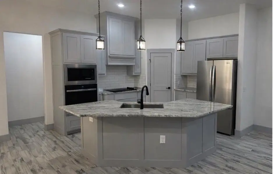 Kitchen featuring gray cabinetry, stainless steel appliances, light stone countertops, and a kitchen island with sink