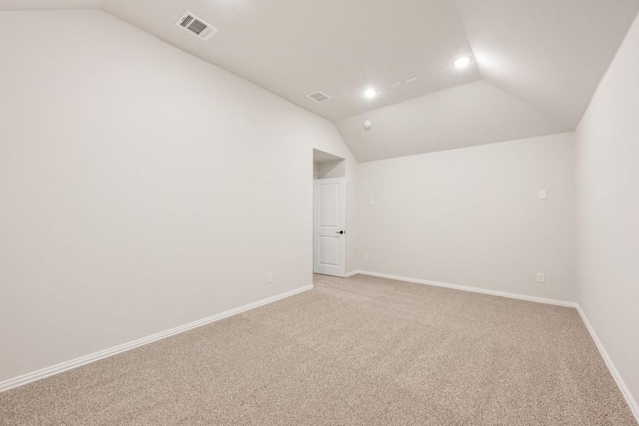 Empty bedroom with vaulted ceiling, beige carpet, white walls, and recessed lighting