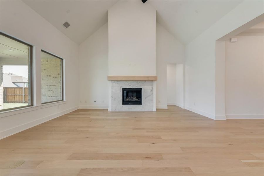 Unfurnished living room with high vaulted ceiling, a premium fireplace, and light wood-type flooring