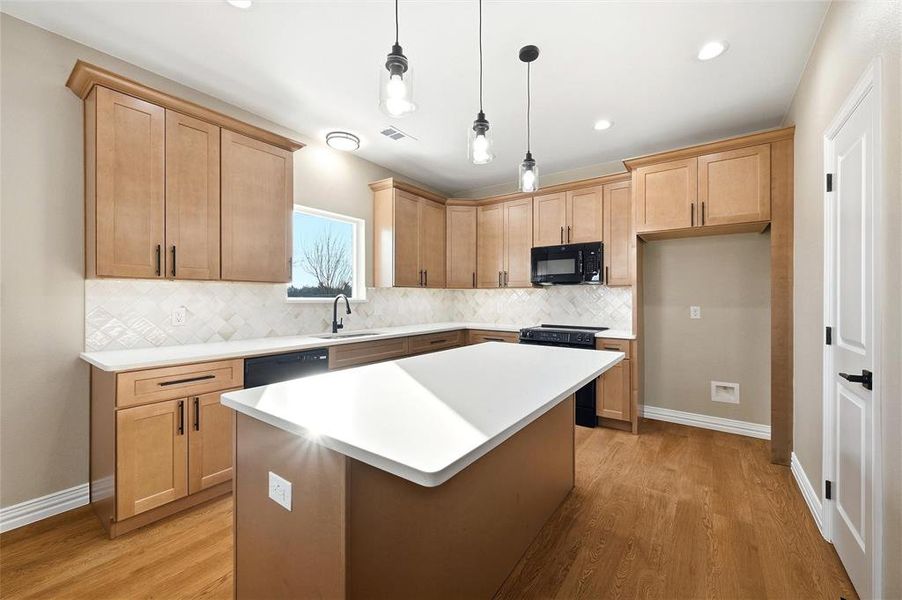 Kitchen with a center island, hanging light fixtures, black appliances, light wood-style flooring, and light wood finish cabinets Kitchen with a center island, hanging light fixtures, black appliances, light wood-style flooring, and light wood finish cabinets