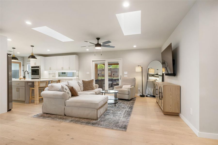 Living room with ceiling fan, light wood-style floors, a skylight, and recessed lighting