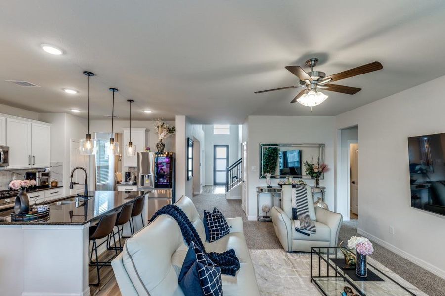 Open-concept living space featuring a sleek kitchen with a large island and bar seating, adjacent to a cozy living area with comfortable seating and contemporary decor. The space is bright and welcoming, enhanced by stylish lighting and a ceiling fan.