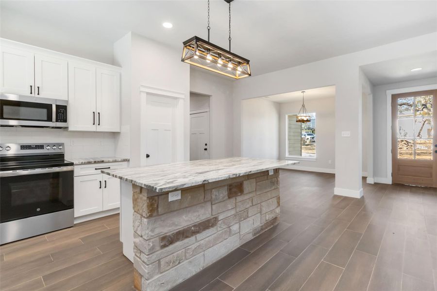 Kitchen featuring hanging light fixtures, appliances with stainless steel finishes, a kitchen island, light stone countertops, and white cabinets