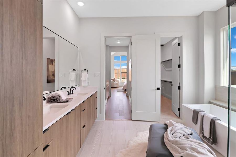 Dual vanity with undermount sinks and matte black fixtures, full-width mirror, built-in storage cabinetry, white soaking tub, and tile flooring