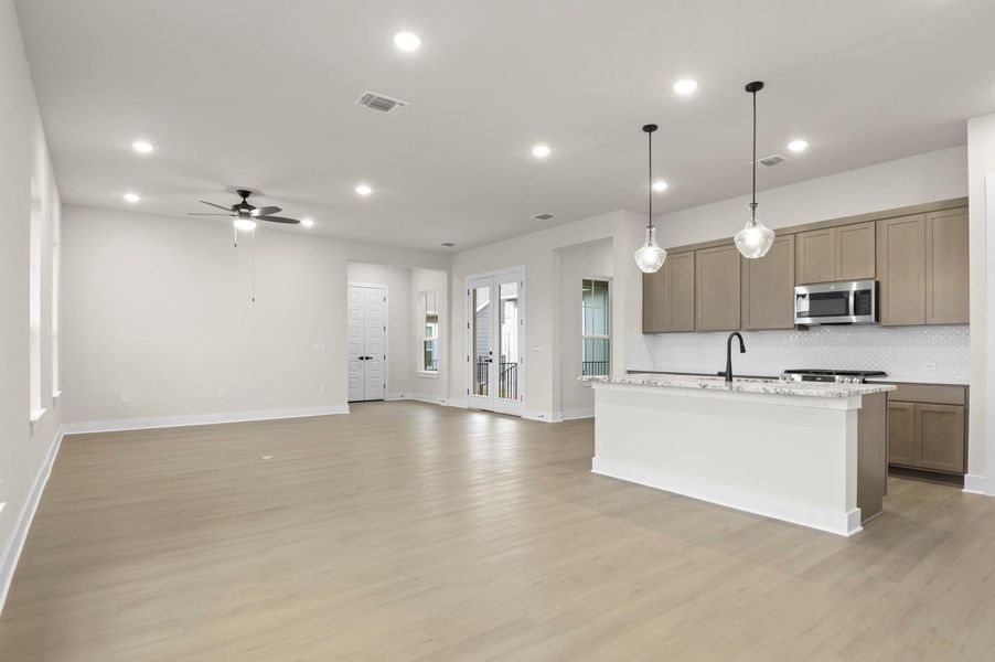 Kitchen featuring open floor plan, a center island with sink, pendant lighting, light wood-style flooring, and recessed lighting