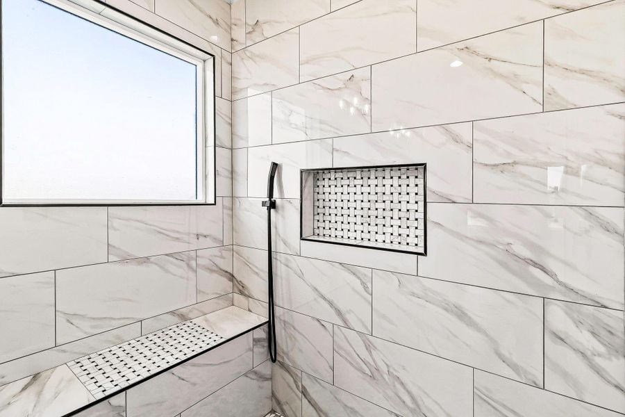 This photo showcases a modern shower with elegant white marble-style tiles, a built-in bench, and a sleek recessed shelf. There's a large window for natural light. This photo showcases a modern shower with elegant white marble-style tiles, a built-in bench, and a sleek recessed shelf. There's a large window for natural light.