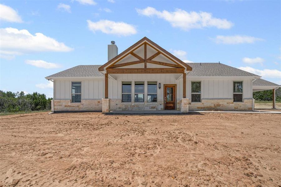 Back of house featuring roof with shingles, board and batten siding, stone siding, and a chimney