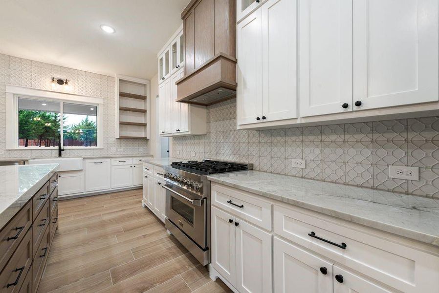 Kitchen with white cabinets, high end stainless steel range oven, decorative backsplash, and light wood-type flooring