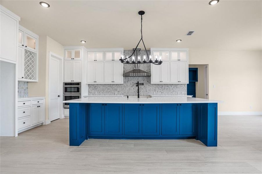 Kitchen featuring stainless steel double oven, a chandelier, light wood-style flooring, a large island, and decorative backsplash Kitchen featuring stainless steel double oven, a chandelier, light wood-style flooring, a large island, and decorative backsplash