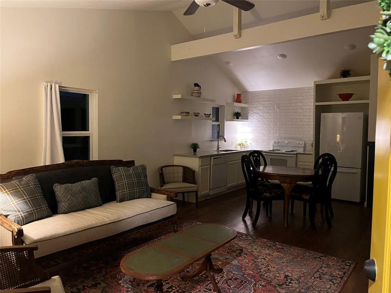 Vaulted ceiling living area featuring wood-finish flooring, an open-concept kitchen with white subway tile backsplash, and built-in shelving