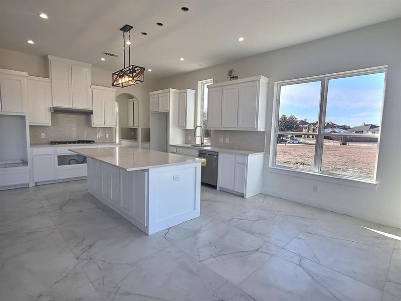 Kitchen with tasteful backsplash, a center island, stainless steel dishwasher, hanging light fixtures, and white cabinets