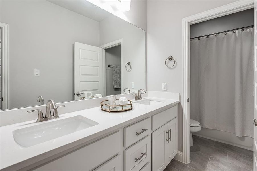 Bathroom featuring tile patterned flooring, toilet, and double sink vanity