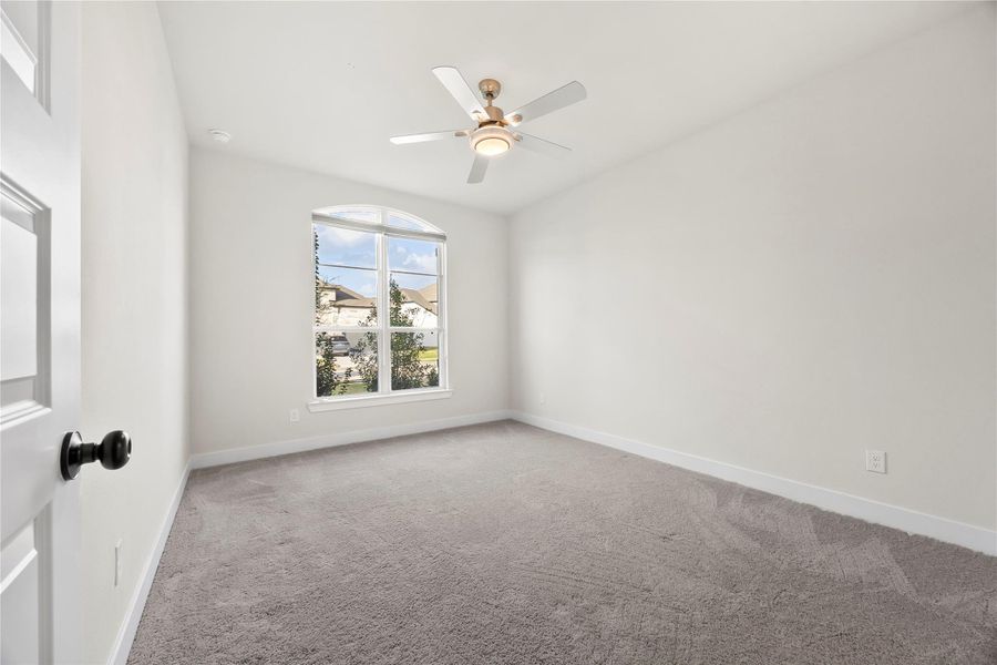 Bright bedroom downstairs with neutral walls, plush carpeting, and a large arched window offering natural light. Ceiling fan for added comfort. Bright bedroom downstairs with neutral walls, plush carpeting, and a large arched window offering natural light. Ceiling fan for added comfort.
