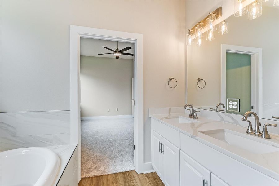 Full bath featuring double vanity, wood finished floors, a ceiling fan, and a tub