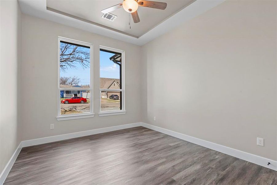 Empty room with ceiling fan, hardwood / wood-style flooring, and a tray ceiling