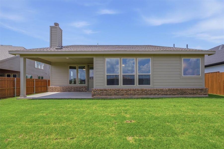 Expansive green lawn bordering a single-story home featuring a covered patio, brick foundation, and multiple windows