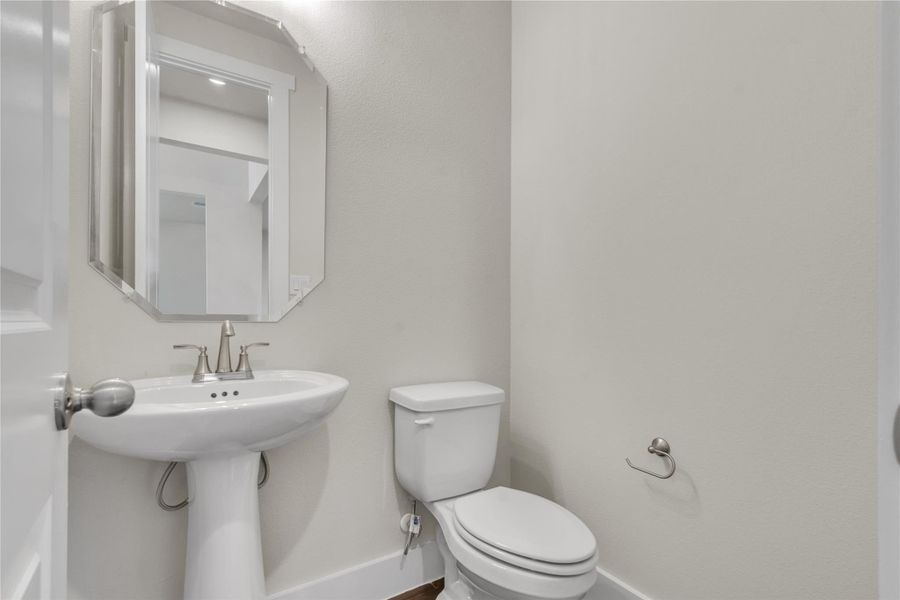 A pristine powder room offers a sleek pedestal sink and contemporary wall mirror.