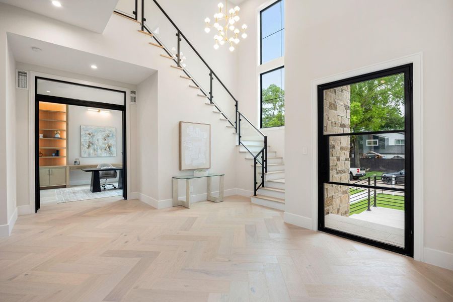 A dramatic entry sets the tone with soaring ceilings, wide-plank flooring, and a sculptural staircase featuring sleek metal and glass detailing. Natural light pours in through oversized windows, enhancing the airy, open feel. Just off the foyer, a private study with custom built-ins offers a quiet retreat, while the open layout draws you deeper into the home with a sense of flow and intentional design throughout.