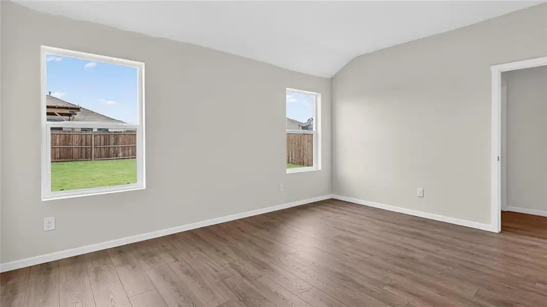 Spacious room featuring vaulted ceilings, two windows, wood-finish flooring, light gray wall paint, and white baseboards