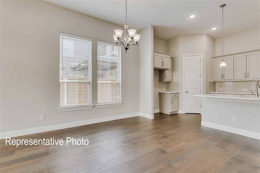 Open-concept interior featuring wood-finish flooring, two large windows with blinds, a five-light chandelier, a kitchen island with pendant lighting, and light-toned cabinetry