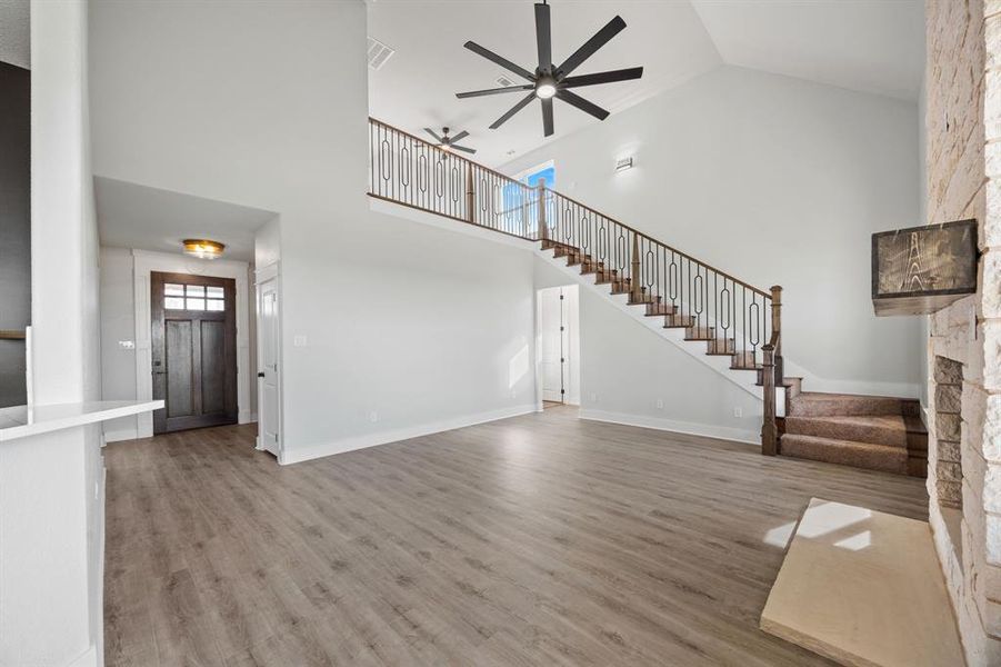 Unfurnished living room featuring light wood-style flooring, stairs, high vaulted ceiling, and a ceiling fan