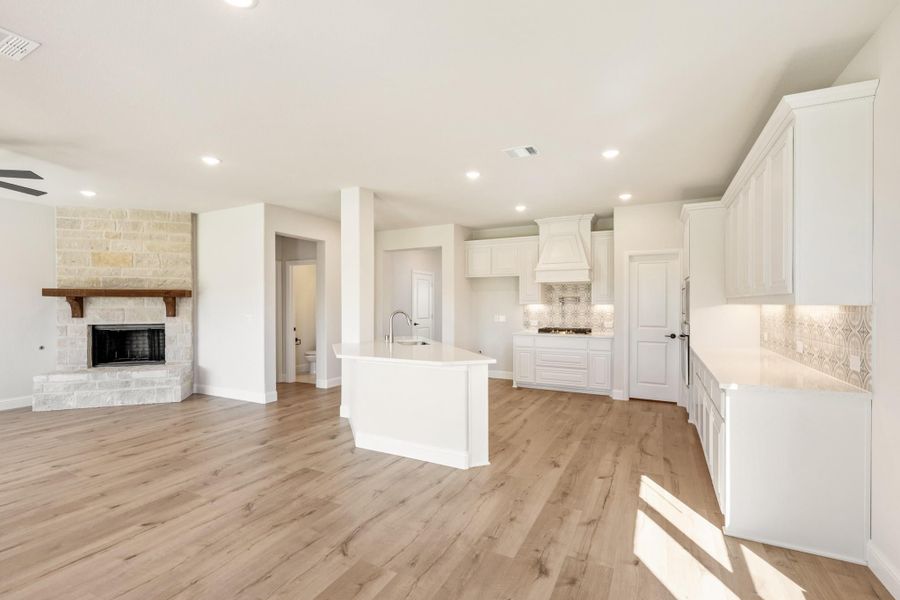 Open-concept kitchen and living area with white cabinets, center island, stone fireplace, and light wood floors