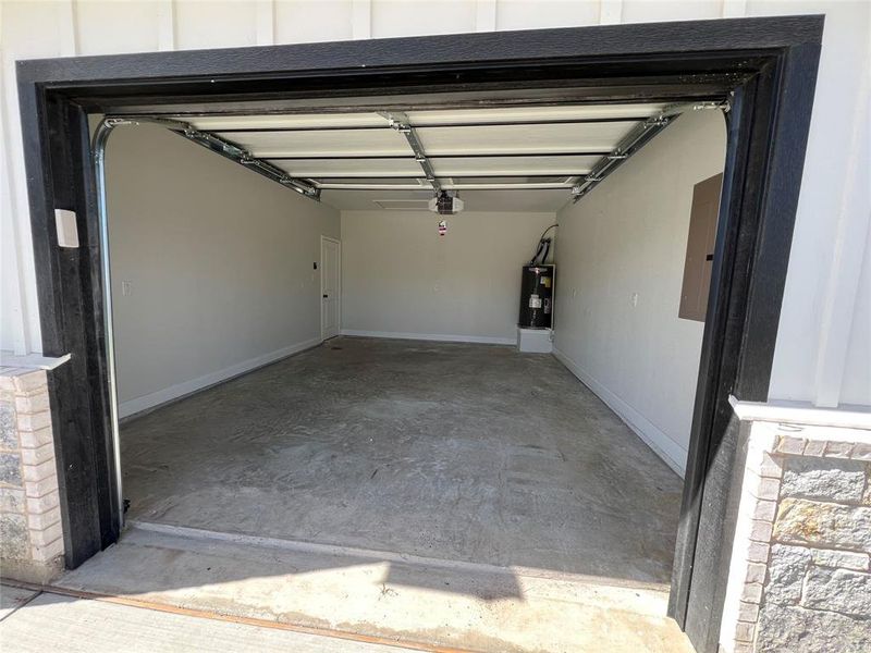 Garage featuring water heater, baseboards, a garage door opener, and electric panel