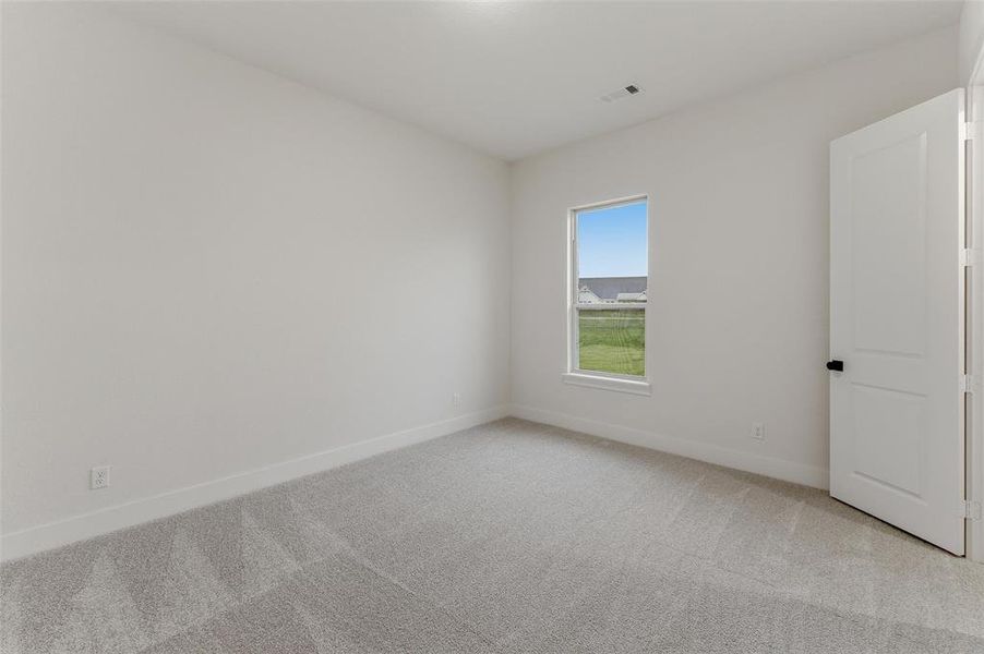 Bedroom featuring light gray carpeting, neutral wall tones, a single window with white trim, and a white interior door with matte black hardware Bedroom featuring light gray carpeting, neutral wall tones, a single window with white trim, and a white interior door with matte black hardware