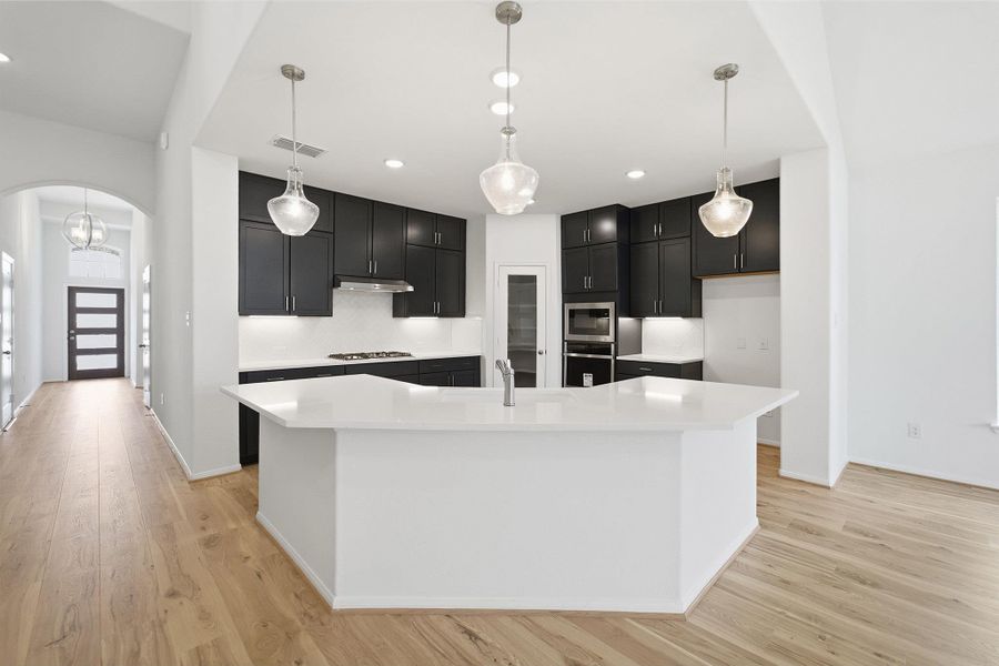 Kitchen with arched walkways, hanging light fixtures, dark cabinetry, light wood-style floors, and light stone counters