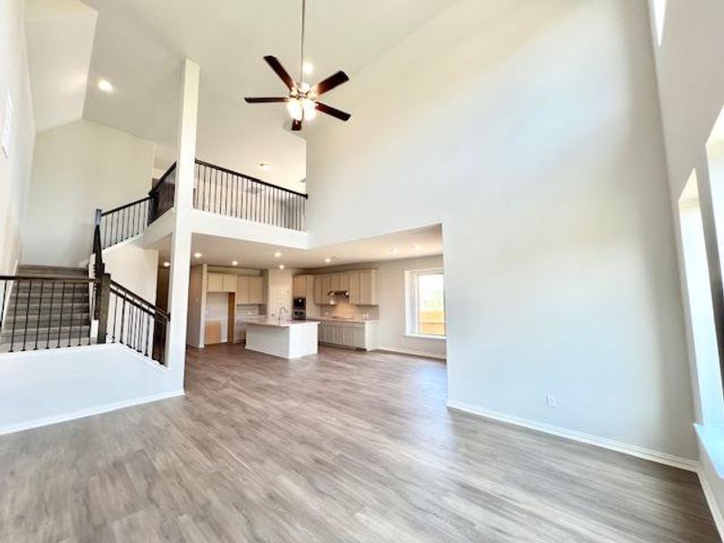 Unfurnished living room featuring light wood-style flooring, high vaulted ceiling, ceiling fan, stairway, and recessed lighting Unfurnished living room featuring light wood-style flooring, high vaulted ceiling, ceiling fan, stairway, and recessed lighting