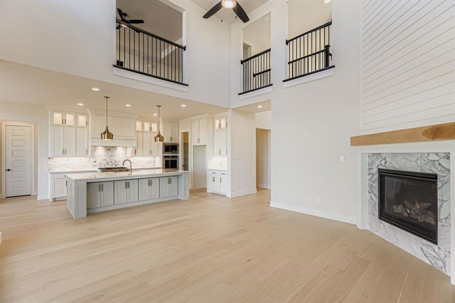Unfurnished living room featuring a fireplace, a ceiling fan, a high ceiling, light wood finished floors, and recessed lighting