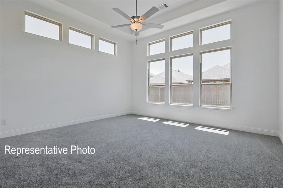 Spacious room featuring high ceilings, gray carpet flooring, multiple large windows, three transom windows, and a ceiling fan with integrated lighting