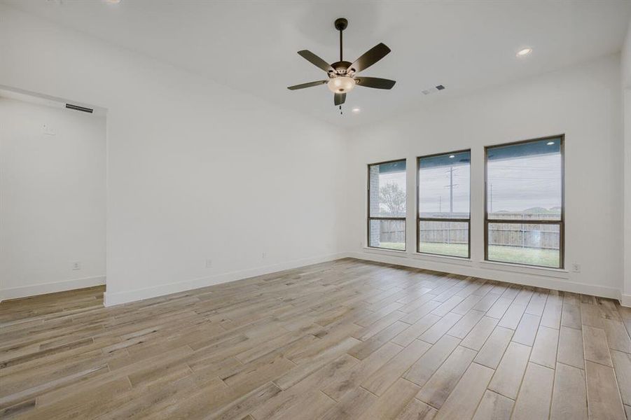 Spacious interior room featuring wood-finish flooring, a contemporary ceiling fan, recessed lighting, and three large windows