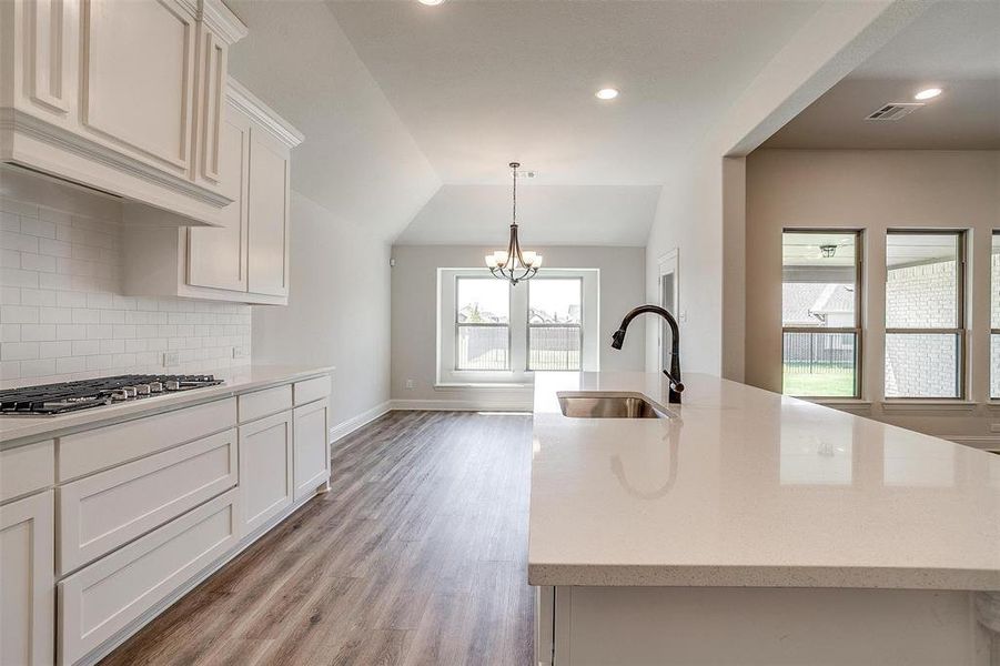 Kitchen with stainless steel gas stovetop, sink, light hardwood / wood-style floors, lofted ceiling, and backsplash