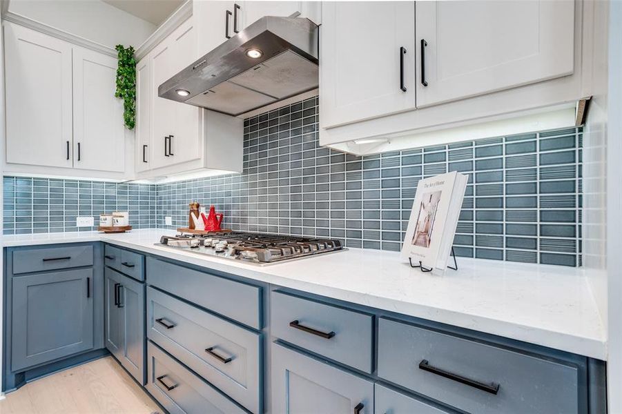 Two tone kitchen featuring two tone cabinets, ventilation hood, light stone counters, stainless steel gas stovetop, and light wood-style flooring