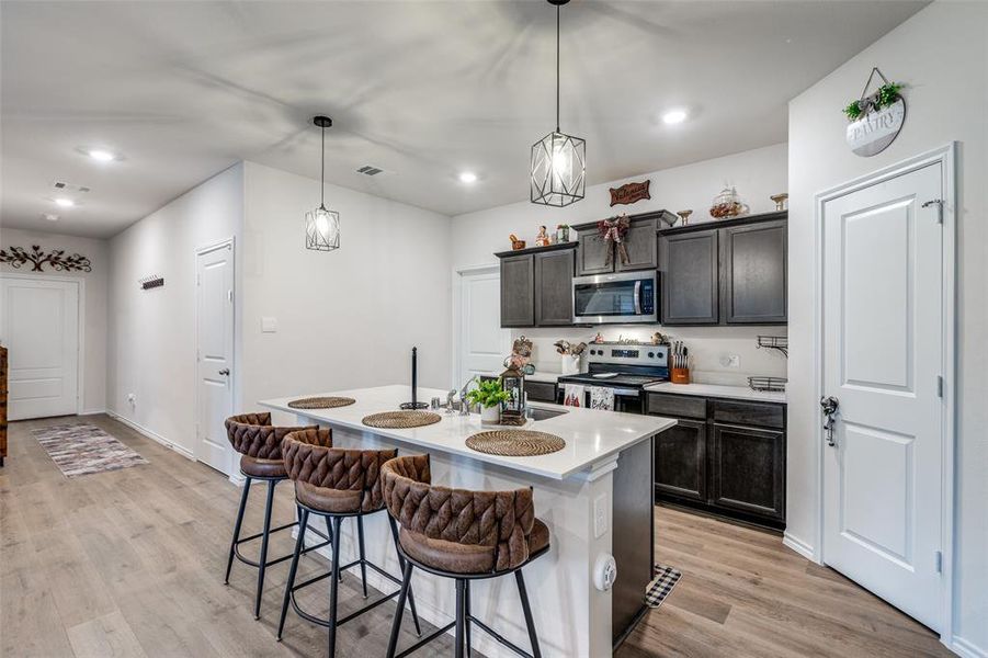 Kitchen with a kitchen breakfast bar, hanging light fixtures, appliances with stainless steel finishes, a center island with sink, and light wood-type flooring Kitchen with a kitchen breakfast bar, hanging light fixtures, appliances with stainless steel finishes, a center island with sink, and light wood-type flooring