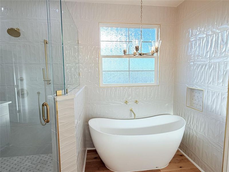 Full bathroom featuring a soaking tub, a shower stall, tile walls, a chandelier, and light wood-style floors Full bathroom featuring a soaking tub, a shower stall, tile walls, a chandelier, and light wood-style floors