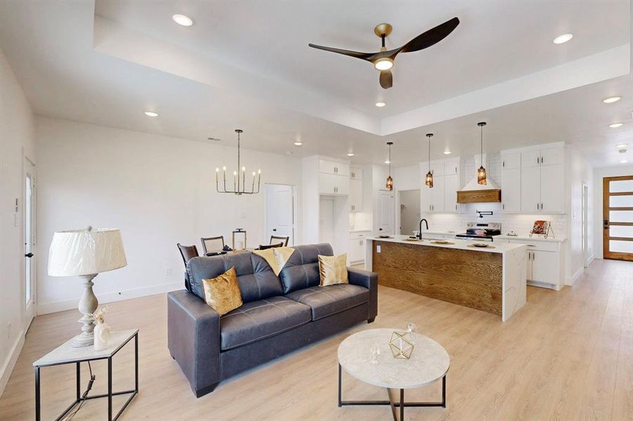 Living room with sink, light wood-type flooring, a tray ceiling, and ceiling fan with notable chandelier