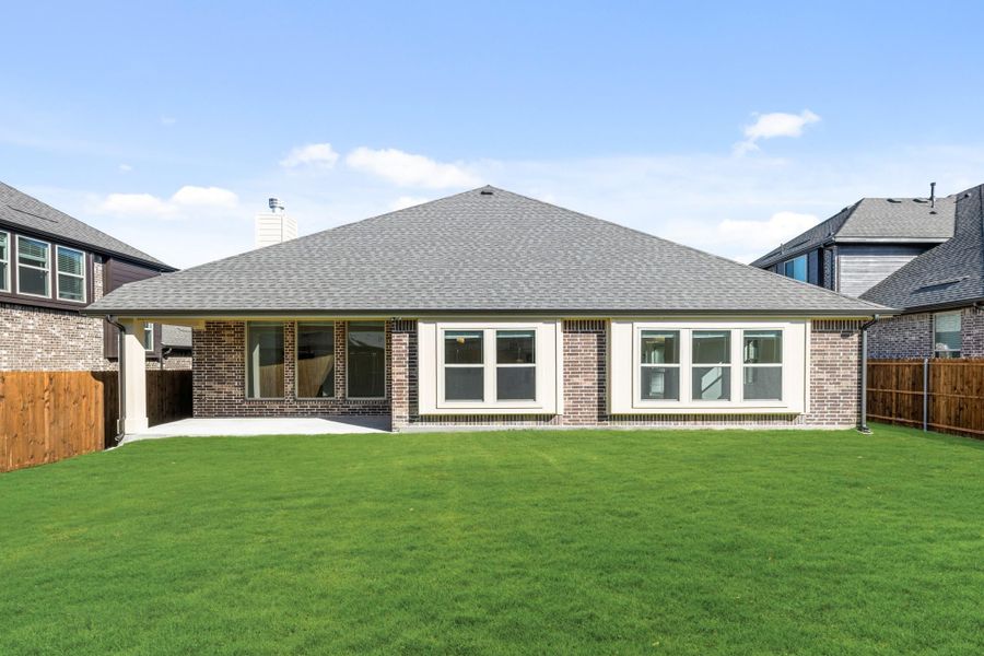 Rear view of single-story brick home with large windows, covered patio, and fenced green backyard Rear view of single-story brick home with large windows, covered patio, and fenced green backyard