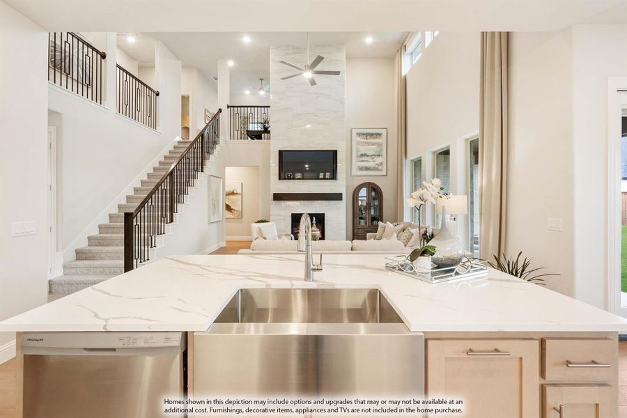 Open-concept kitchen with marble island and farmhouse sink overlooking two-story living room with fireplace and staircase