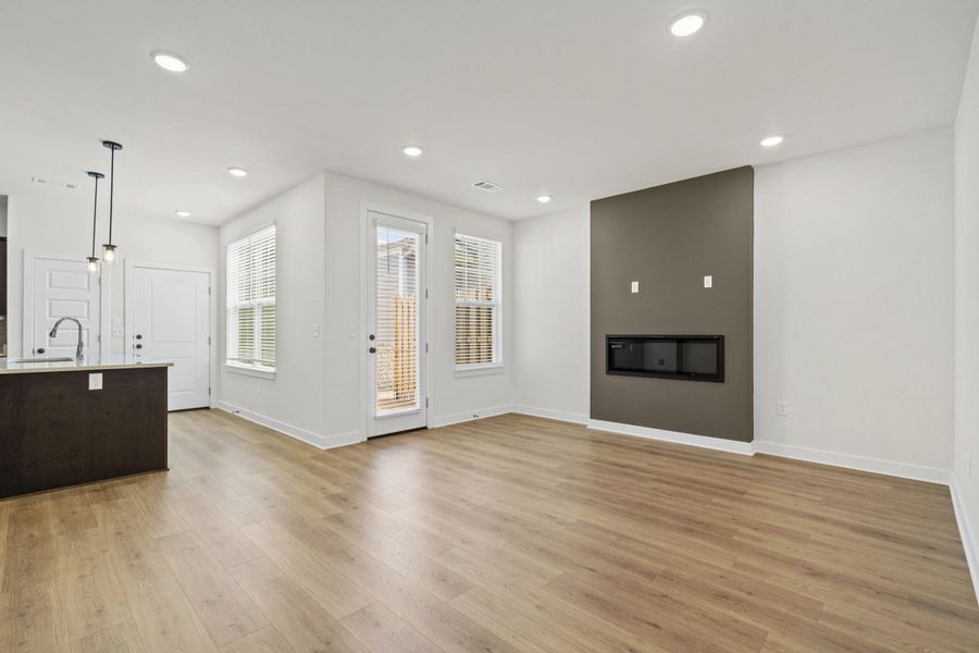 Open-concept living space with wood-finish flooring, recessed lighting, and a modern fireplace feature wall